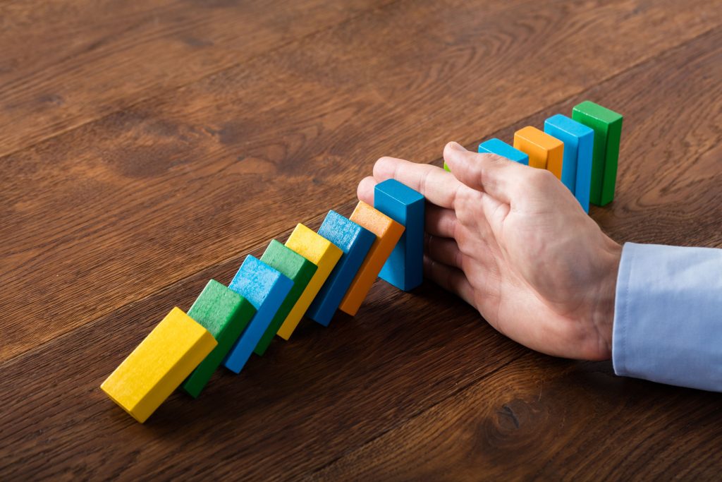 Image of a hand stopping a line of domino pieces form falling - represents that you should learn the truth about budgets and stop doing things that don't work